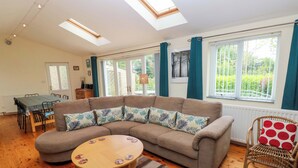 A living room with a sectional sofa, a round wooden coffee table, and a dining area with a table and chairs. - Greenbanks (Newport)