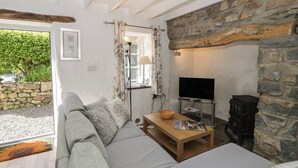 A cozy living room with a stone wall, a sofa, a television, and a fireplace. - Middle Cottage (Newport)
