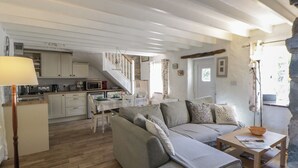 A cozy living room with a sofa, a dining table, and a kitchen area with a staircase. - Middle Cottage (Newport)