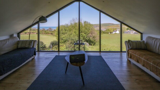 Une pièce avec un plafond en pente, un canapé, un fauteuil et une vue sur un paysage verdoyant.