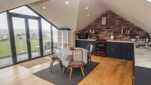 Une cuisine moderne avec un mur de fond en briques, un four encastré et un coin repas comprenant une table et des chaises.