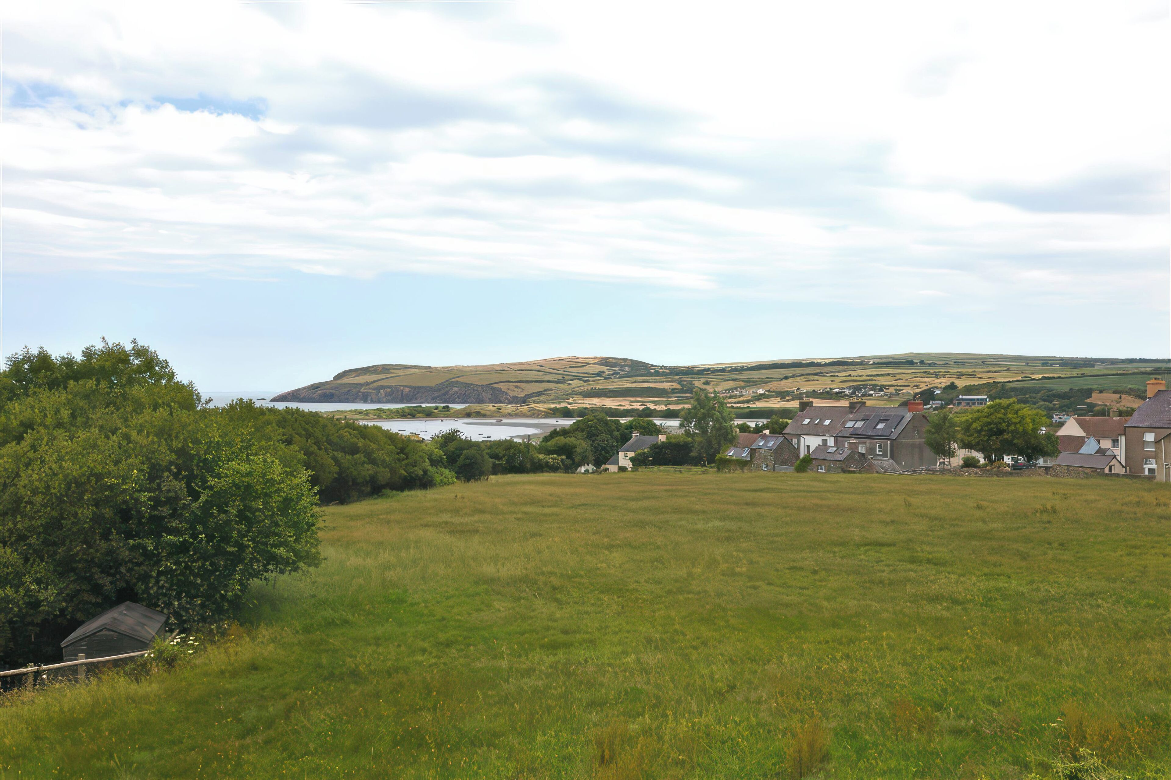 A rural landscape with rolling hills, a body of water, and a cluster of houses.