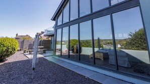 Un bâtiment moderne doté de grandes fenêtres en verre, d’un patio aménagé avec du mobilier d’extérieur et offrant une vue dégagée sur le paysage environnant.