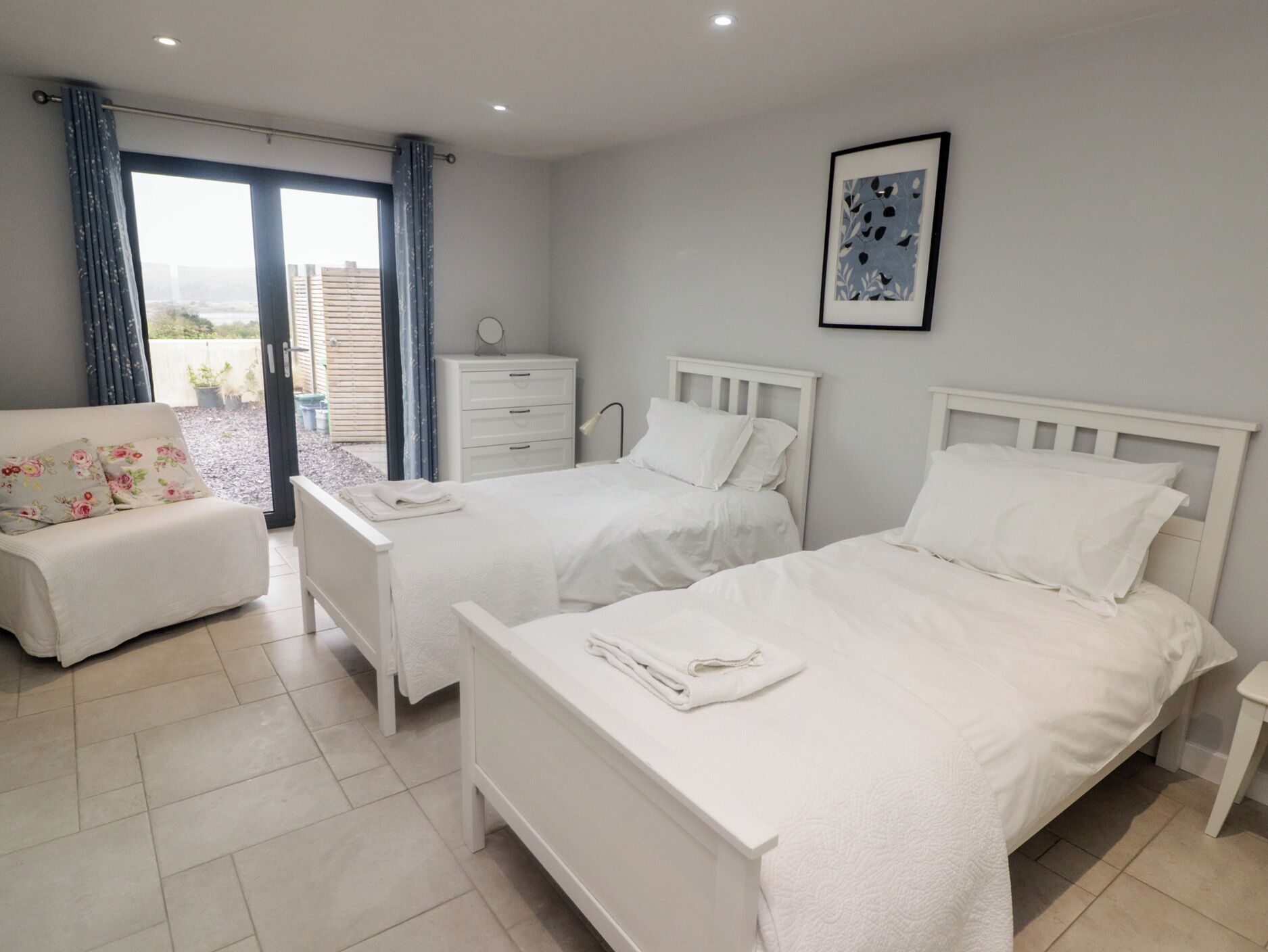 A bedroom with two beds, a sofa, a dresser, and a window with curtains.