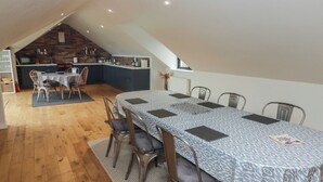 Un espace repas avec une longue table, des chaises et une cuisine en arrière-plan.