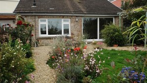 A stone house with a tiled roof, a gravel pathway, and a garden with various plants and flowers. - Gellifor (Cardigan)
