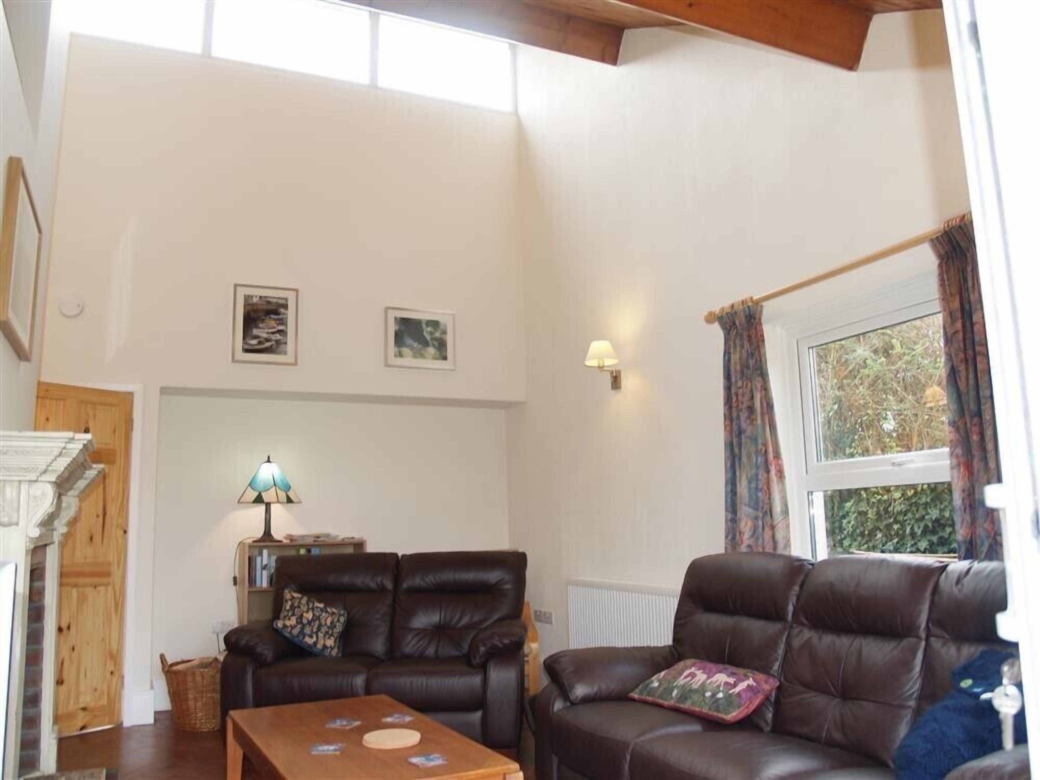 Un salón amplio con dos sofás de cuero, una mesa de centro y una chimenea. Hay dos cuadros en la pared y una ventana con cortinas.