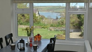 A dining table with a checkered tablecloth, two black chairs, and a window view of a river and greenery. - Gellifor (Cardigan)
