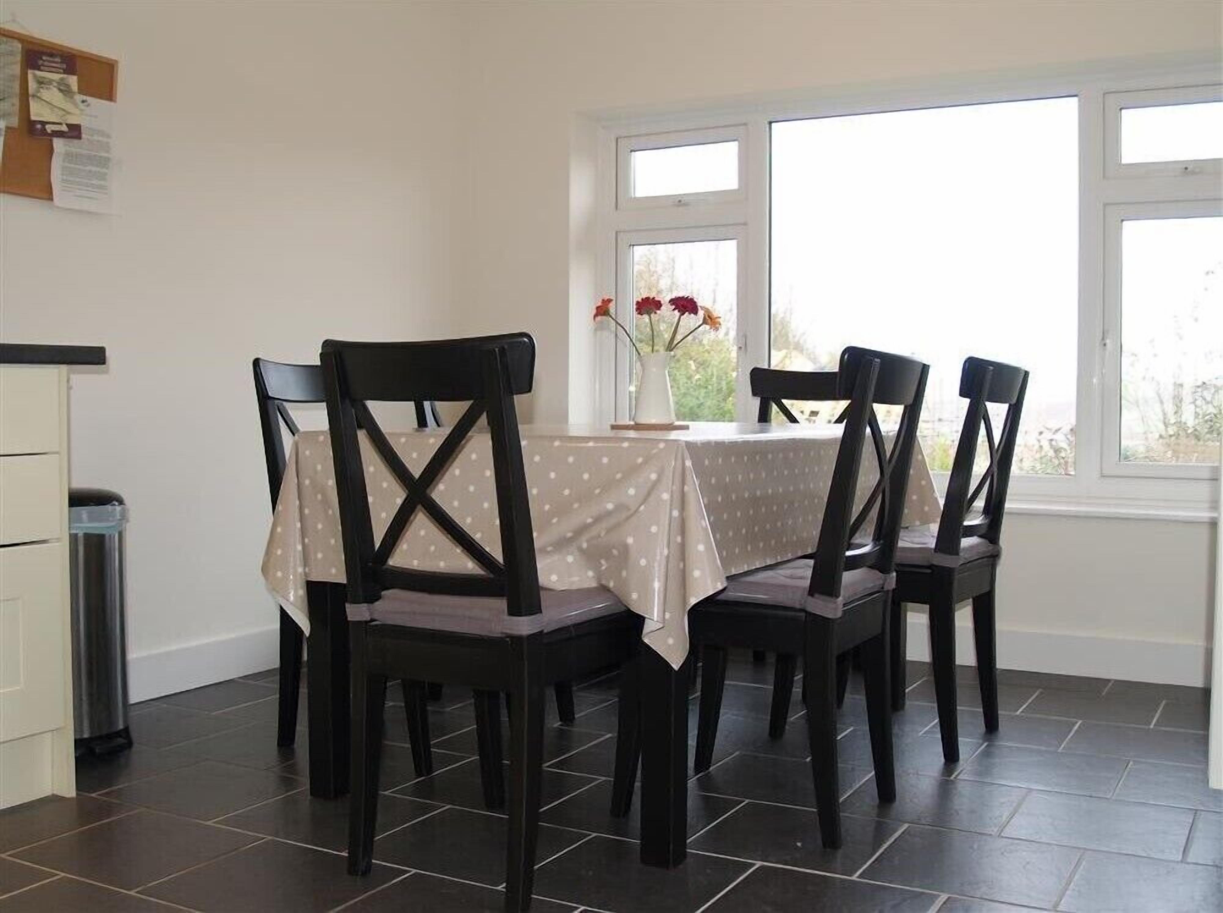 A dining area with a round table covered by a polka dot tablecloth, surrounded by four black chairs with a distinctive back design.