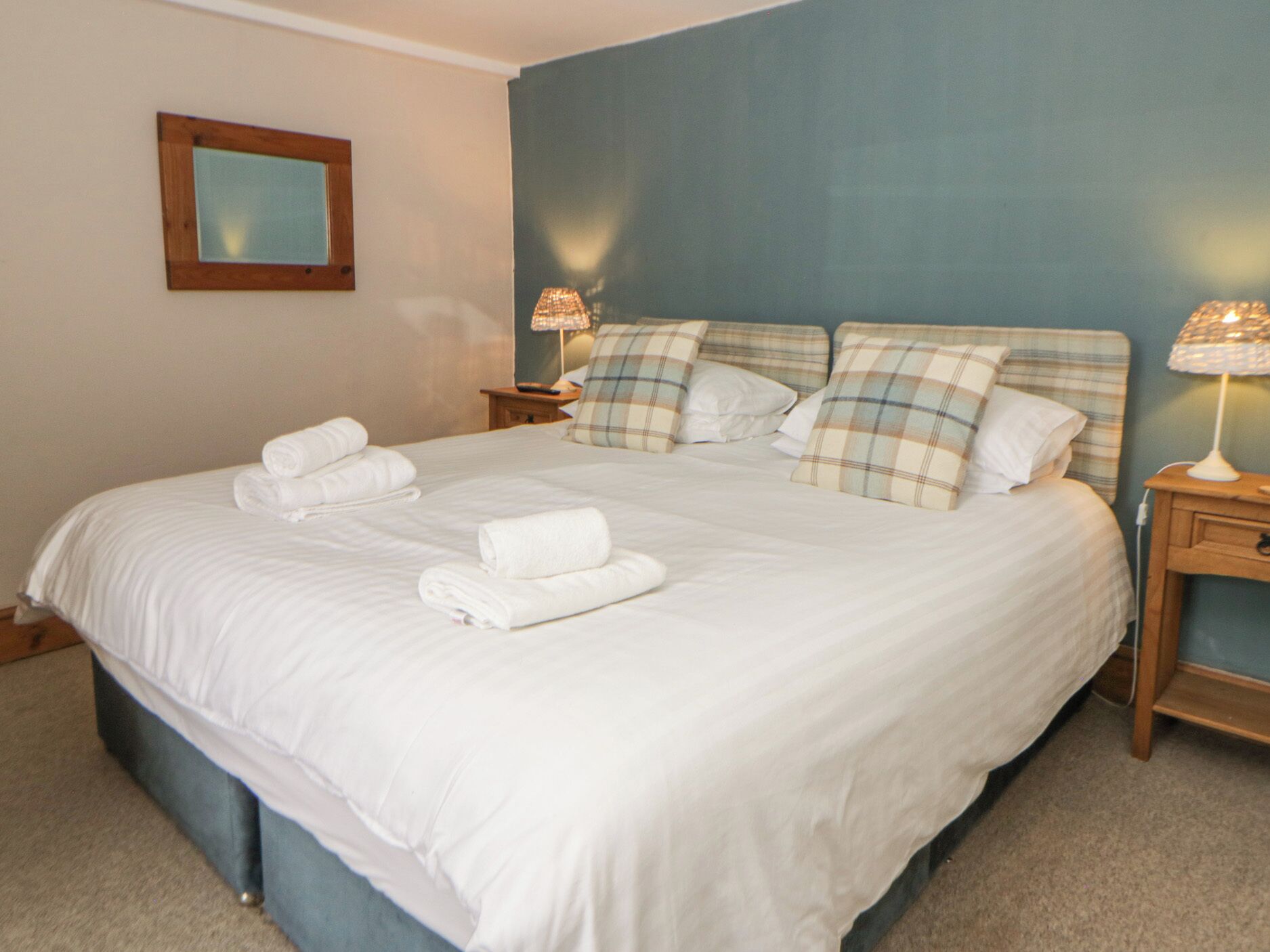 A neatly made bed with white linens and rolled towels, a plaid headboard, and bedside lamps on wooden nightstands.