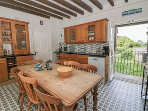 A kitchen with wooden cabinets, a dining table, chairs, and a view of the garden through an open door.