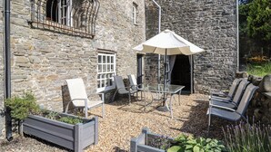 An outdoor seating area with stone walls, a table, chairs, and an umbrella. - Dewi Villa (Aberaeron)