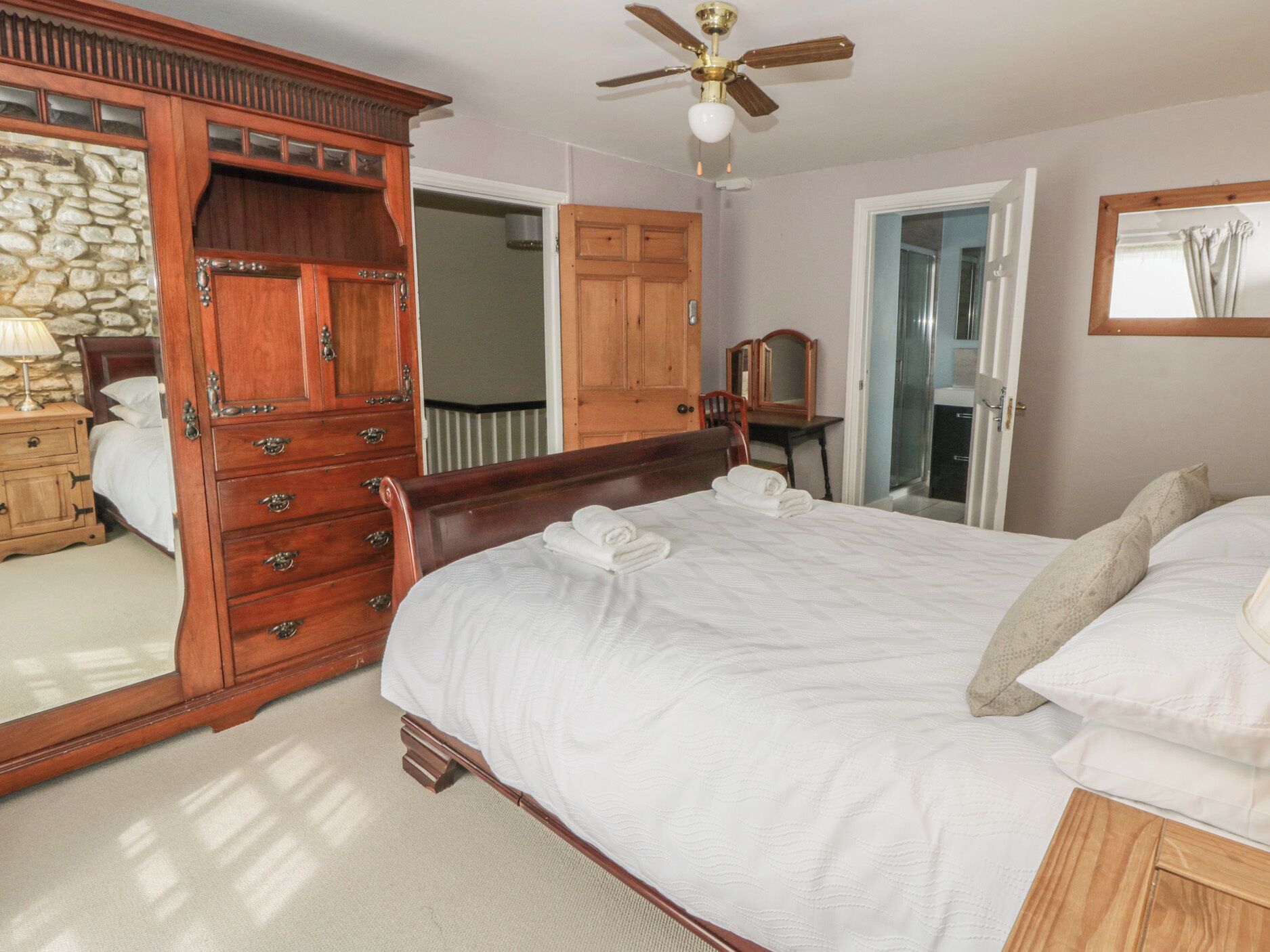 A bedroom with a large bed, wooden wardrobe, and a ceiling fan.