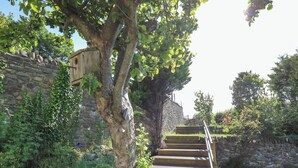 A wooden staircase leading up to a stone wall, surrounded by greenery and trees. - Dewi Villa (Aberaeron)