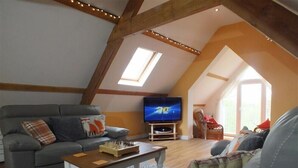A cozy loft-style living room with a grey sofa, a wooden coffee table, and a flat-screen TV. - Pond Cottage (Llandysul)
