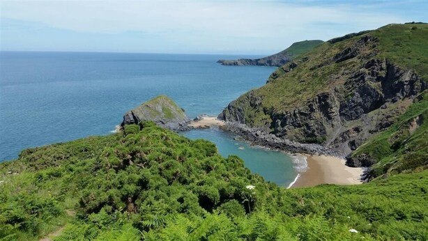 A coastal landscape with a beach, rocky cliffs, and dense greenery. - Pond Cottage (Llandysul)