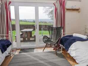 Une chambre avec un lit, une chaise et une vue sur l’extérieur, accessible par une porte vitrée, donnant sur un espace extérieur équipé d’une table de pique-nique.