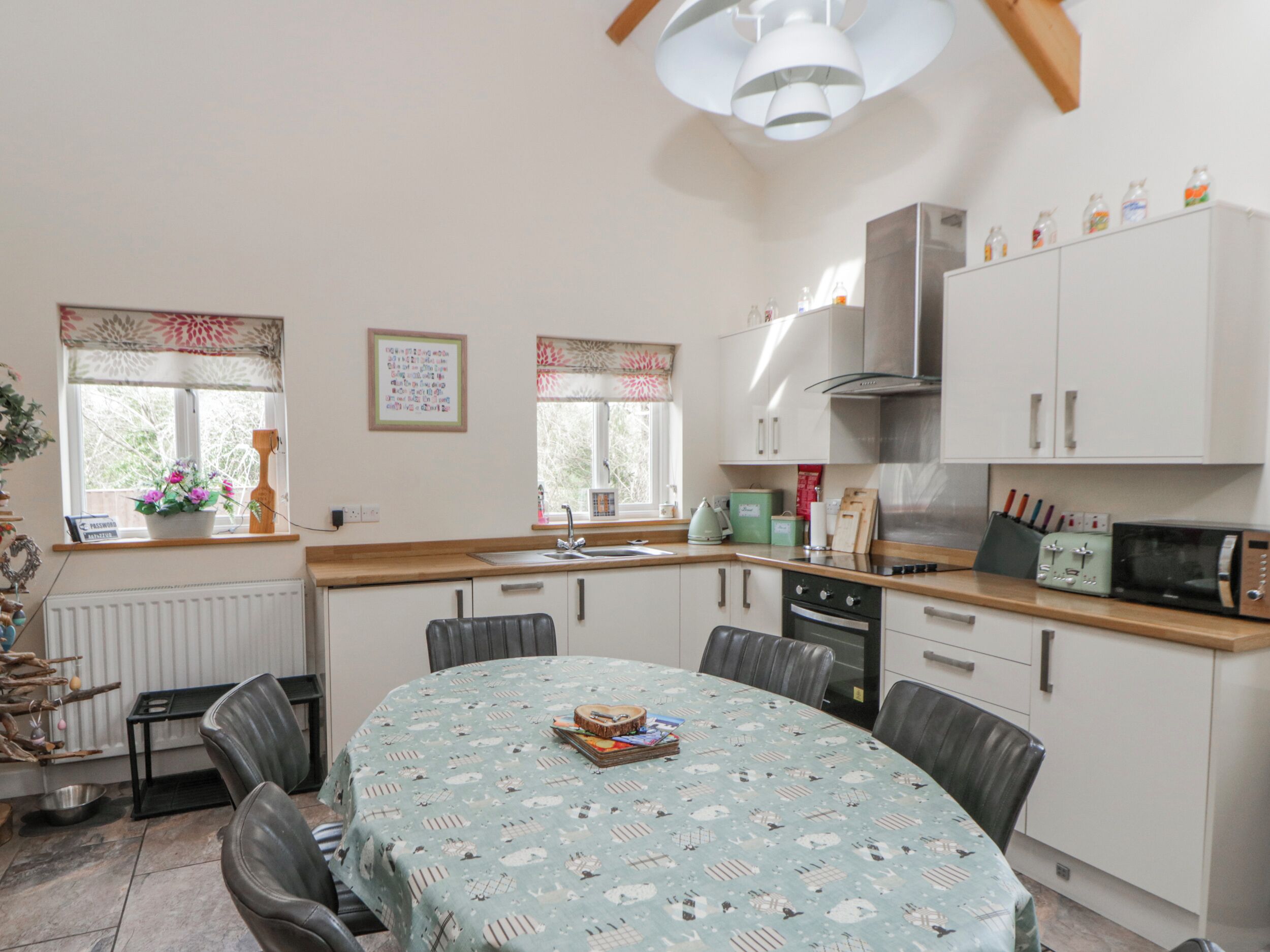 A modern kitchen with white cabinets, a dining table with a patterned tablecloth, and a variety of kitchen appliances.