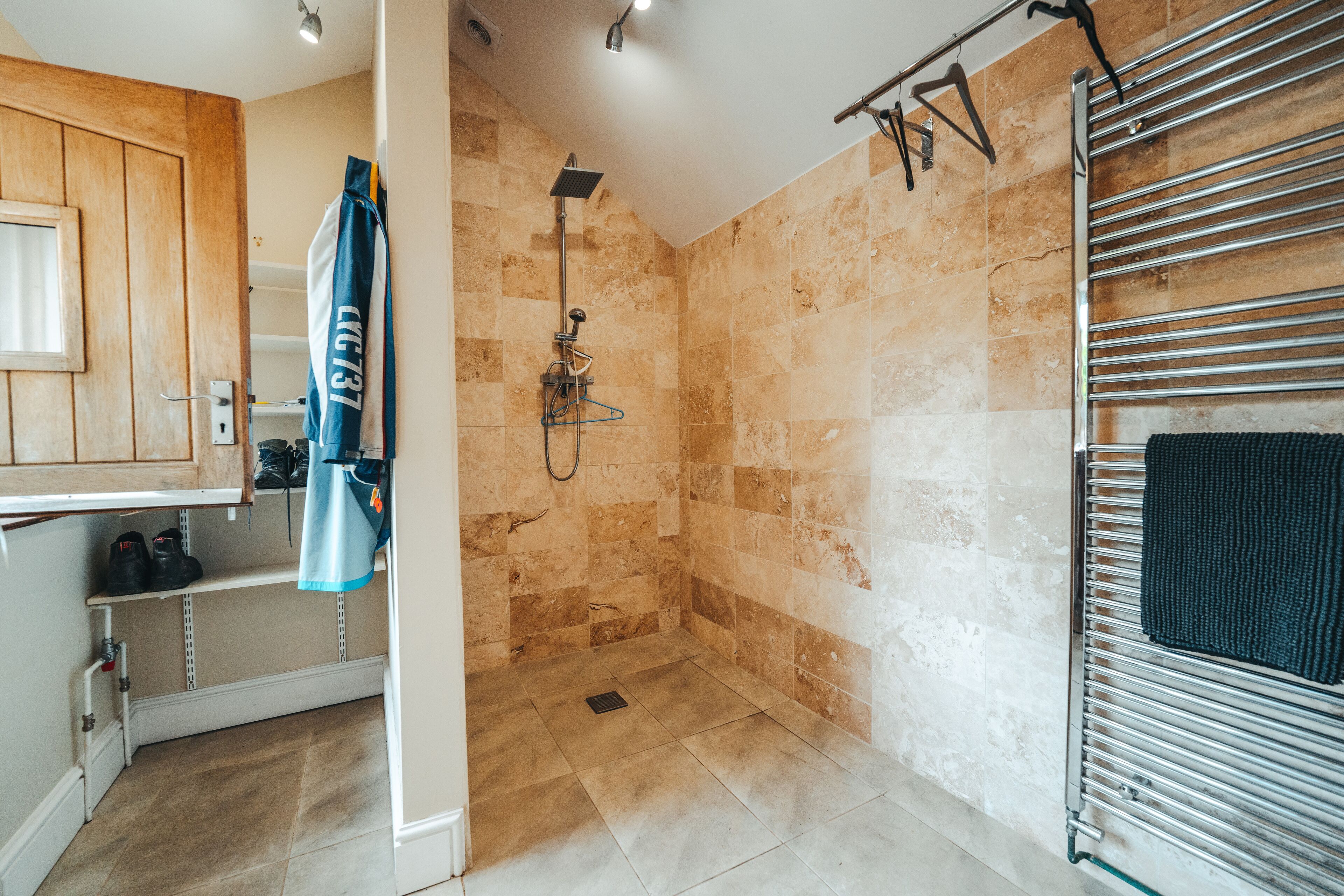 Une salle de bain avec une douche, des murs carrelés, un porte-serviettes et une étagère où sont rangées des chaussures.