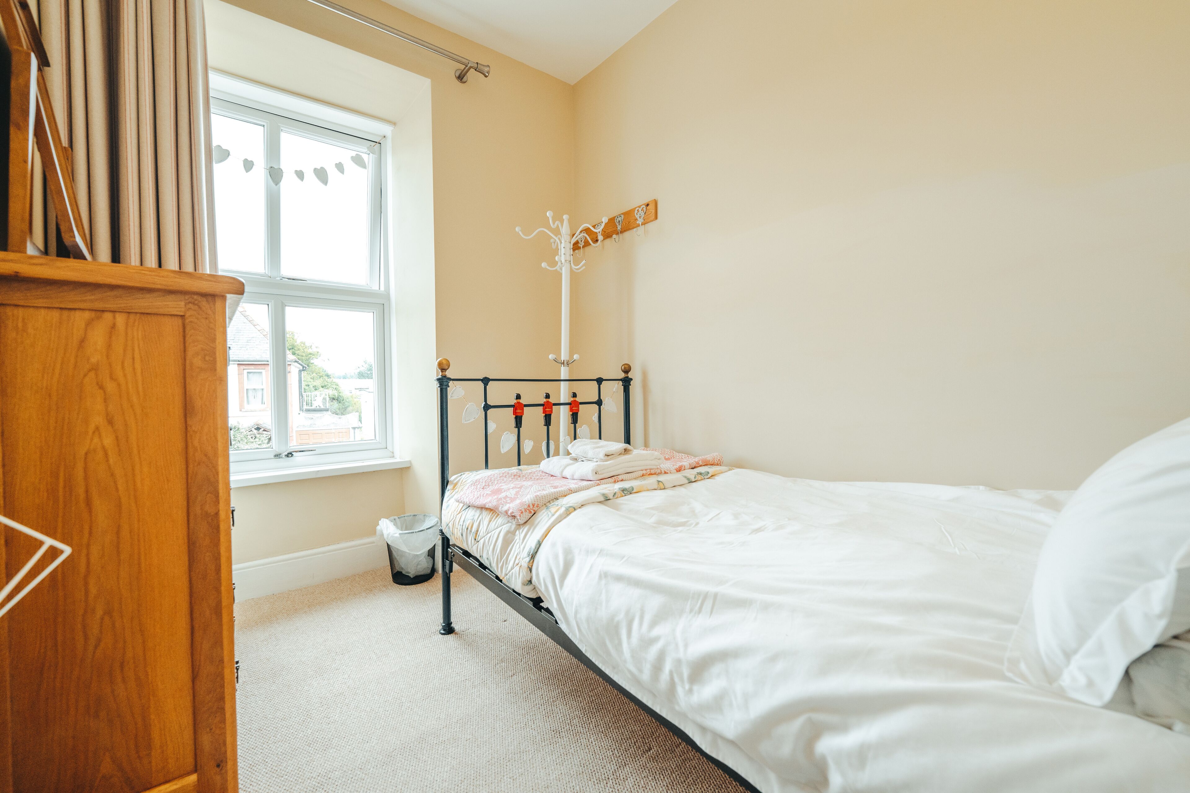 A bedroom with a bed, a wooden wardrobe, a coat rack, and a window with curtains.