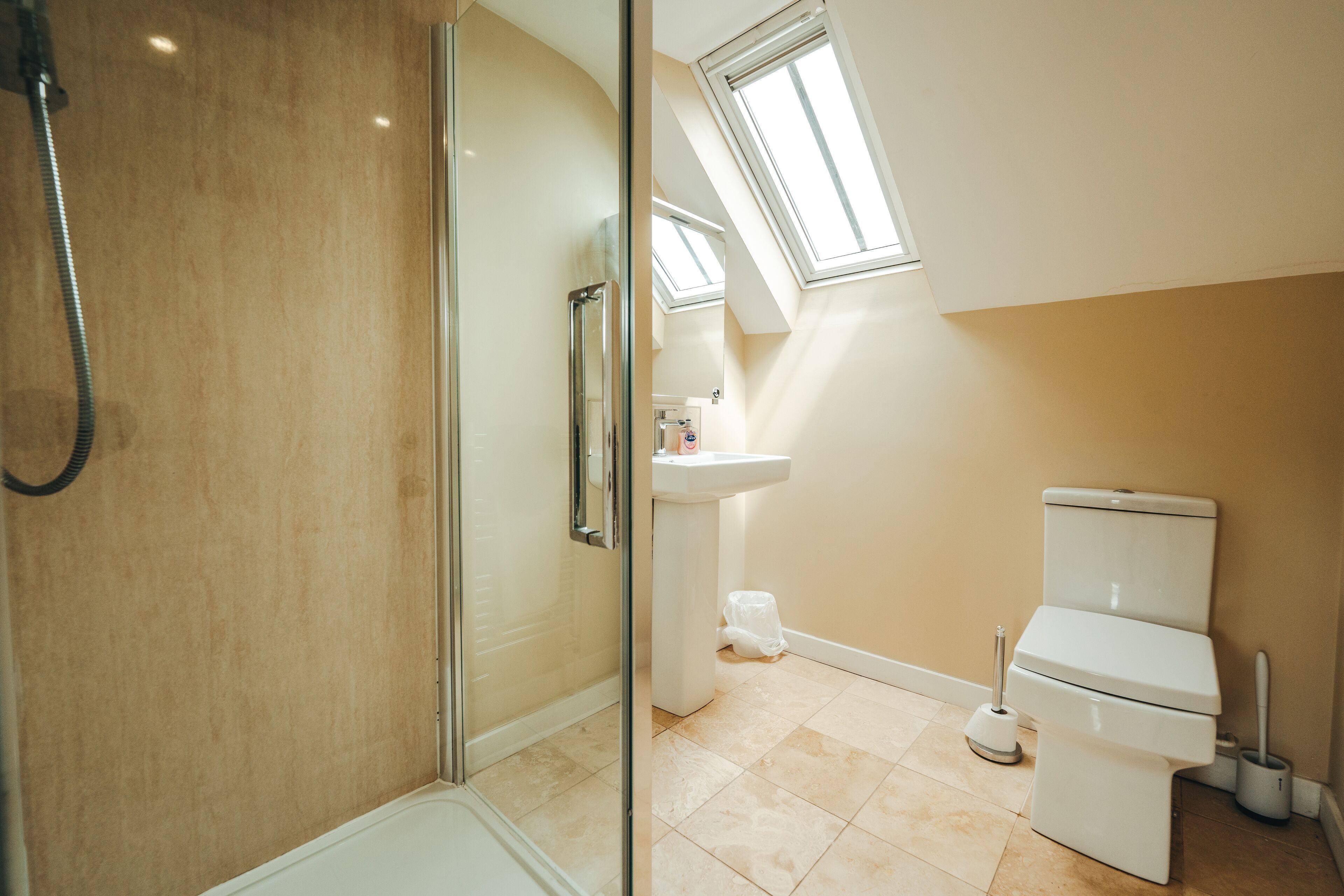 A bathroom with a glass-enclosed shower, a toilet, a sink, and a window providing natural light.