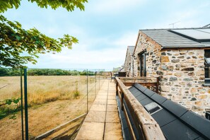 A stone building with a wooden deck and a glass barrier overlooking a field.