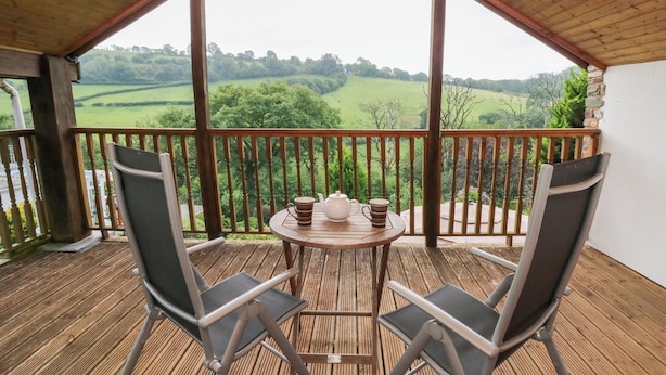 A wooden deck with two chairs and a table, overlooking a green landscape. - Dan Castell Cottage (Llandeilo)