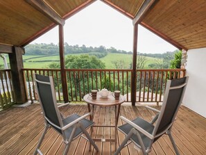 A wooden deck with two chairs and a table, overlooking a green landscape.