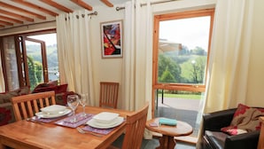 A dining area with a wooden table set for two, a small round table, and a leather sofa. - Dan Castell Cottage (Llandeilo)