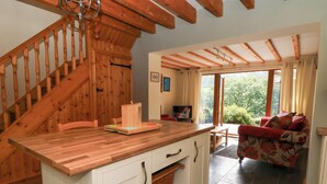 A cozy kitchen with a wooden island, a staircase, and a living area with a sofa and a TV. - Dan Castell Cottage (Llandeilo)