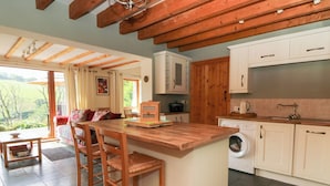 A kitchen with wooden beams, a washing machine, and a dining area with a table and chairs. - Dan Castell Cottage (Llandeilo)