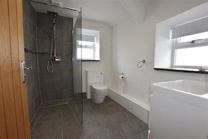 Moderni kylpyhuone, jossa on lasiseinällä varustettu suihku, wc ja kylpyamme.