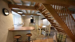 A kitchen with wooden beams, a dining area with a table and chairs, and a staircase. - The Old Farmhouse Kitchen (Haverfordwest)