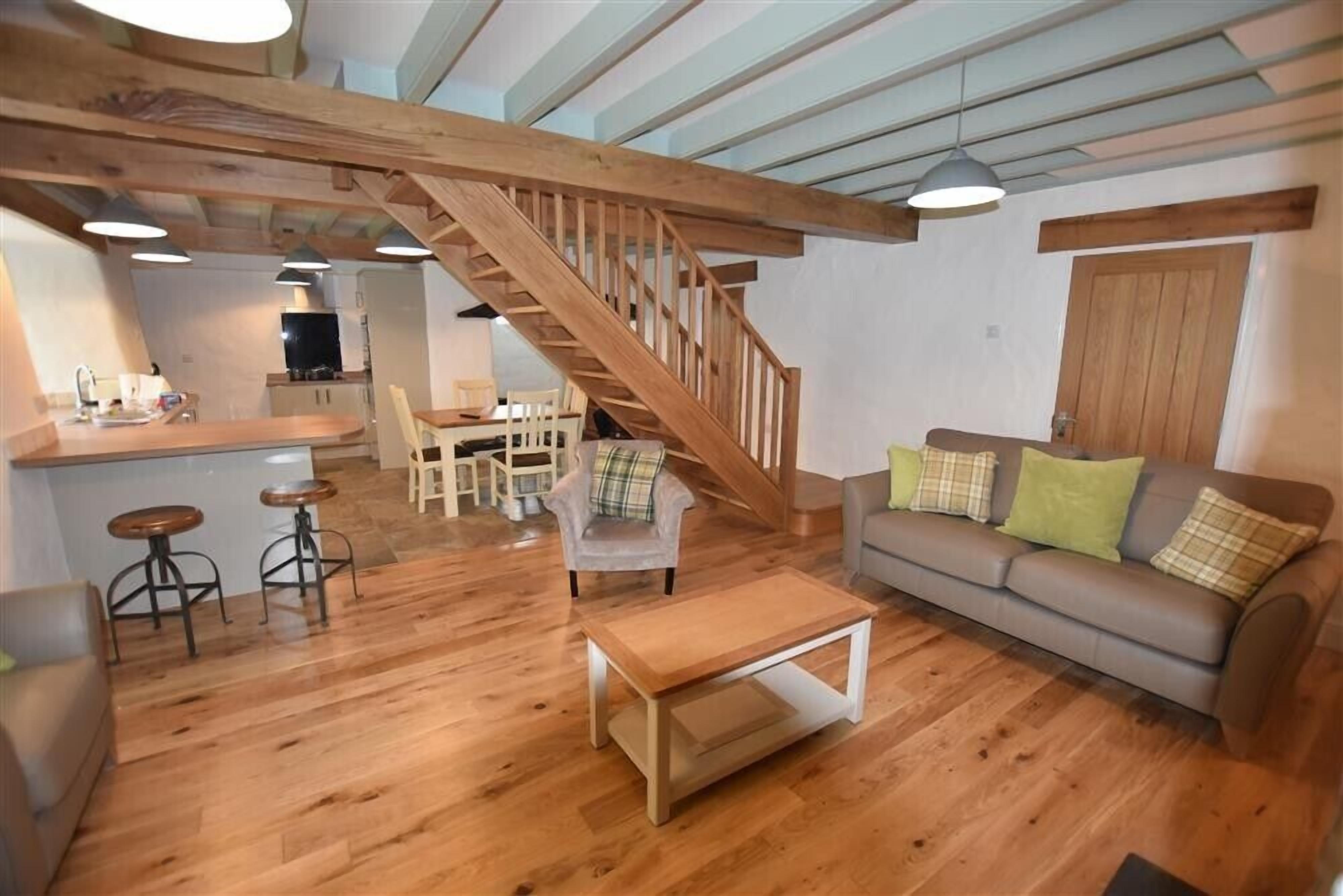 Ein geräumiger Wohnbereich mit einer Holztreppe, einem Sofa, einem Couchtisch und einer Küche im Hintergrund.