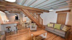 A spacious living area with a wooden staircase, a sofa, a coffee table, and a kitchen in the background. - The Old Farmhouse Kitchen (Haverfordwest)