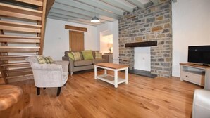 A cozy living room with a stone fireplace, wooden furniture, and a television. - The Old Farmhouse Kitchen (Haverfordwest)