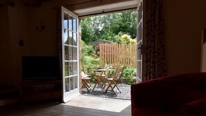 An open door leading to a patio with a table and chairs, a wooden bench, and a television in the adjacent room. - Cwmbrandy Cottage (Fishguard)