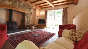 A cozy living room with a stone fireplace, a red sofa, a cream sofa, and a red armchair. - Cwmbrandy Cottage (Fishguard)