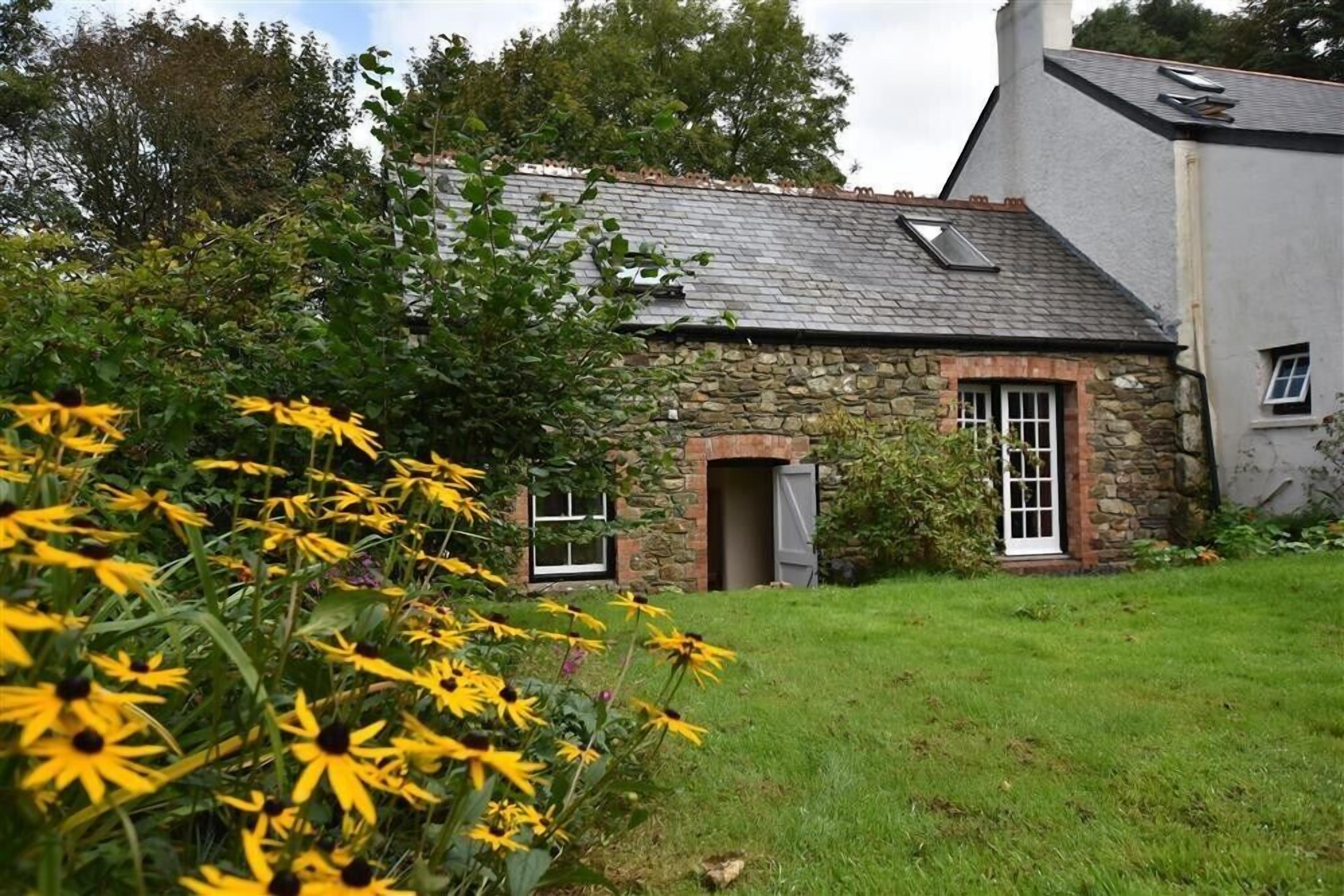 A stone house with a sloped roof, a small garden, and a white door.