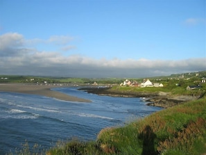 A coastal landscape with a beach, a small settlement, and a clear sky. - Dolwylan (Newport)