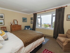 A bedroom with a bed, a dresser, a chair, a window with curtains, and a view of the outside.
