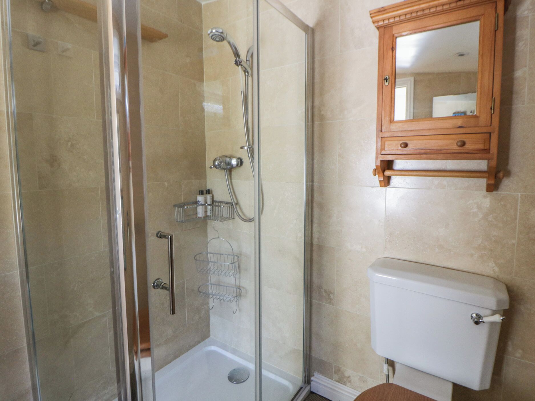 A bathroom with a glass-enclosed shower, a wooden medicine cabinet, and a white toilet.