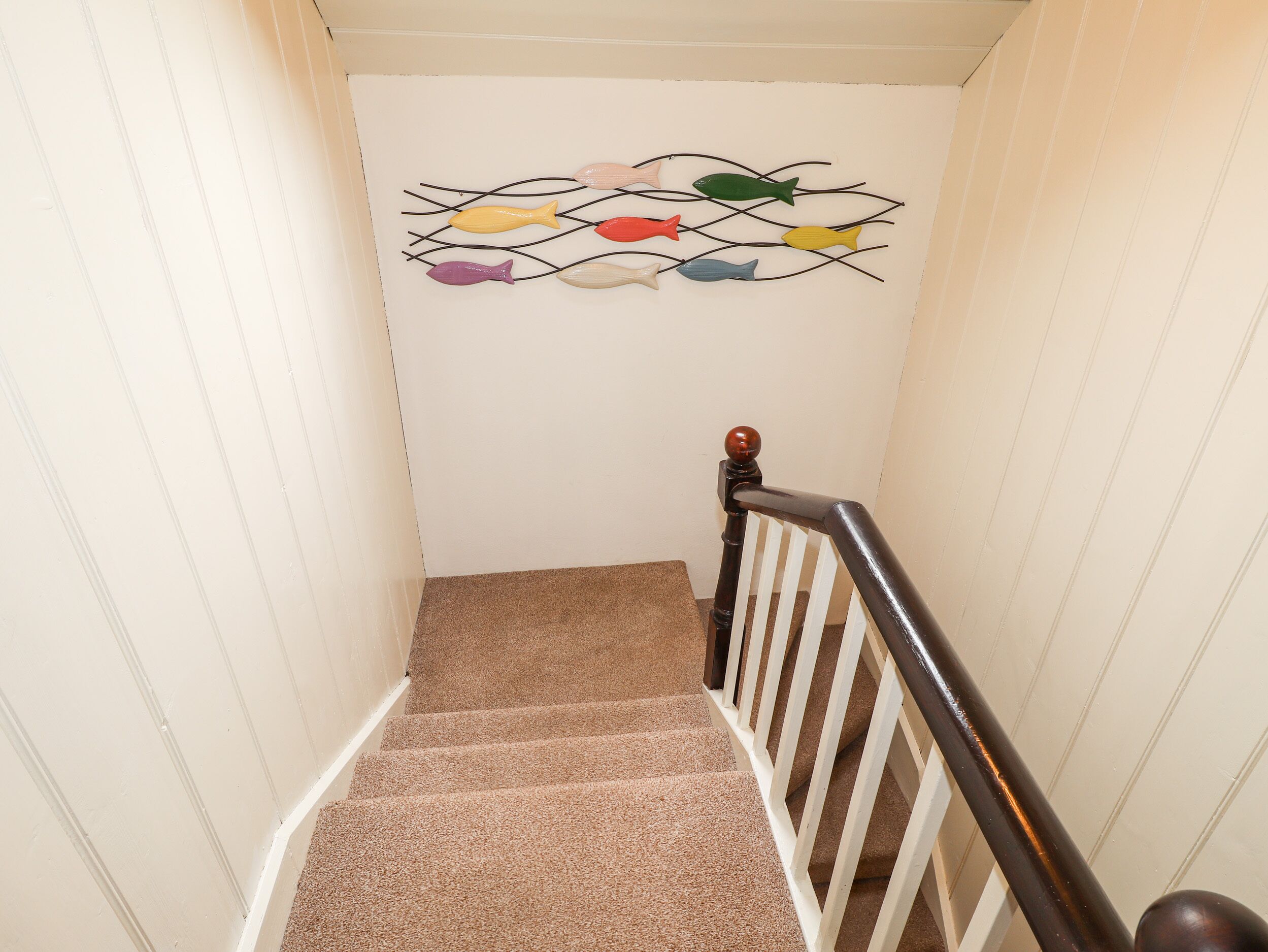 A carpeted staircase with a wooden handrail and a wall-mounted fish decoration.