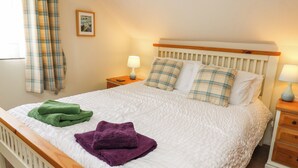 A neatly made bed with plaid pillows, a green and purple towel, and a bedside lamp. - Panteg Cottage, Newport (Newport)