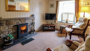 A cozy living room with a stone fireplace, a television, a comfortable armchair, and a window with curtains. - Panteg Cottage, Newport (Newport)