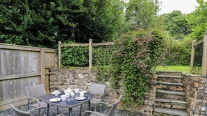 A patio with a round table and four wicker chairs, surrounded by stone steps and a wooden fence. - Panteg Cottage, Newport (Newport)