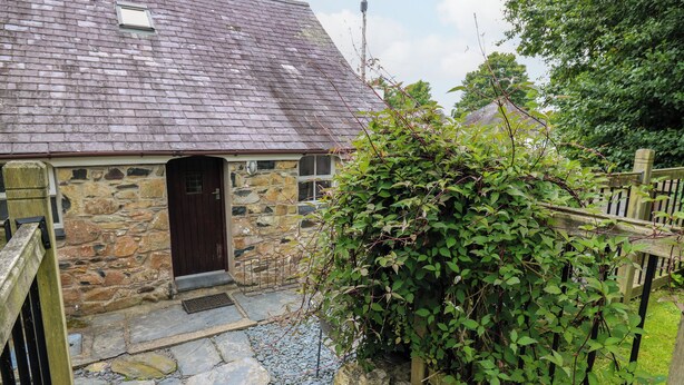 A stone cottage with a dark wooden door, a stone pathway leading to the entrance, and a wooden fence with climbing plants. - Panteg Cottage, Newport (Newport)