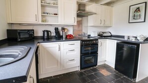 A compact kitchen with white cabinets, a black stove, a microwave, and a dishwasher. - Panteg Cottage, Newport (Newport)