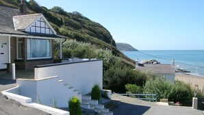 A coastal house with a white exterior, a large bay window, and a view of the sea.