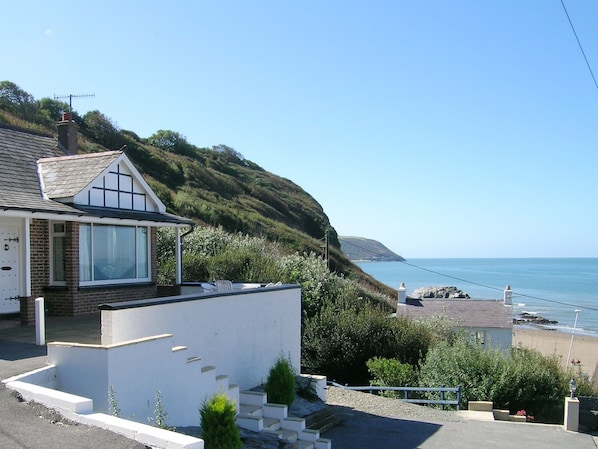 Una casa costera de exterior blanco, con un amplio ventanal y vista al mar.